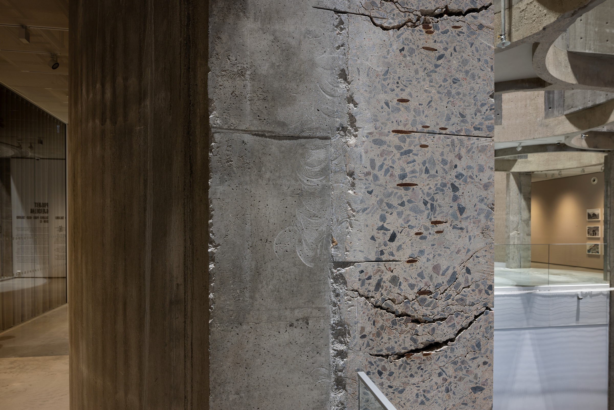 Et nærbilde av en betongsøyle med eksponert tilslag og synlige sprekker står i et innendørs arkitektonisk rom.