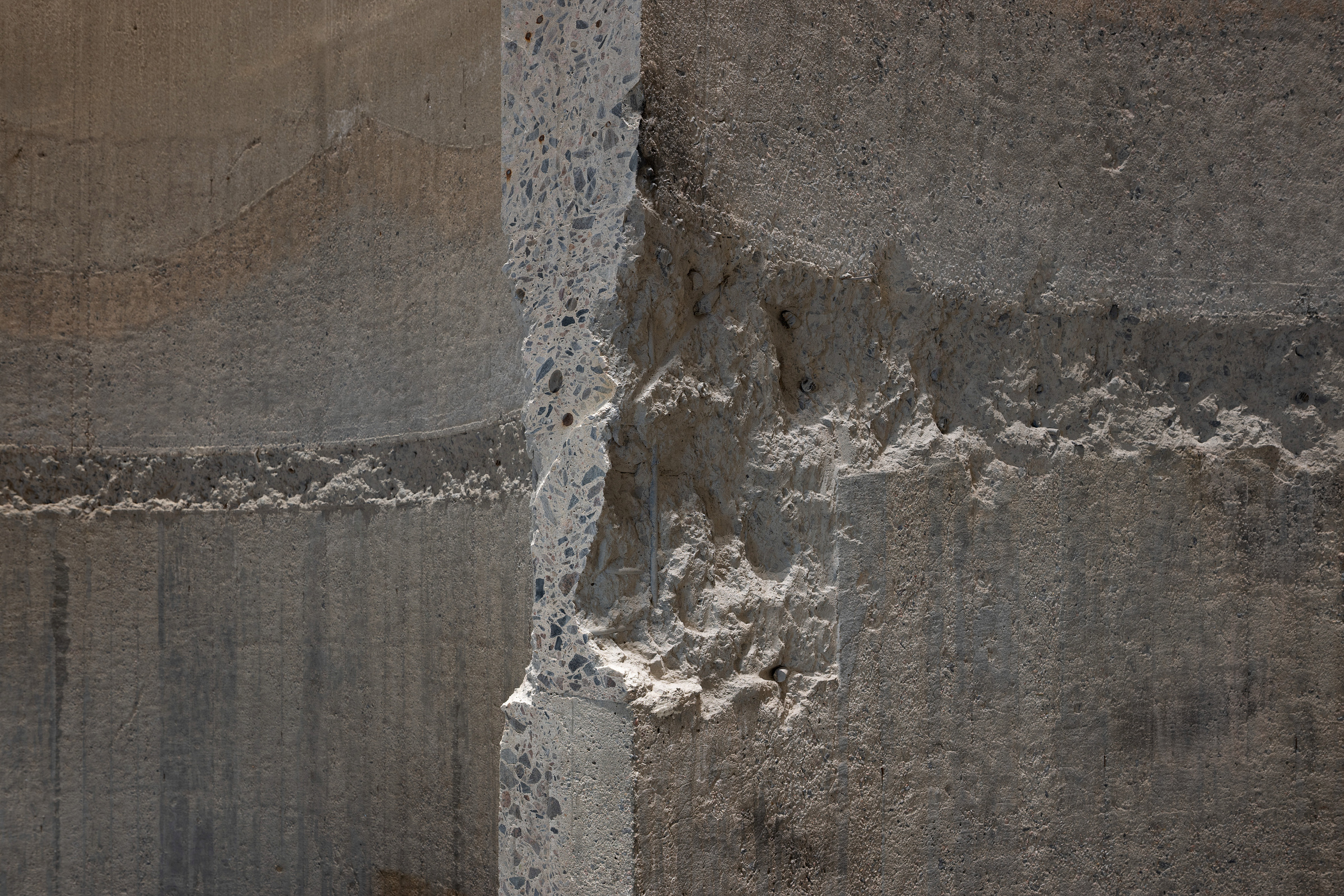 Nærbilde av en betongvegg med et vertikalt snitt som avslører tilslaget på innsiden og ru, skadede områder på overflaten.