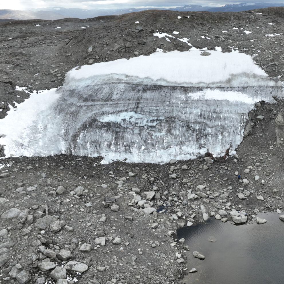 Delte ut 43 millionar til arkeologi – dette var dei mest spanande funna 14 En flekk med smeltende isbre med synlige jordlag er omgitt av steinete terreng, løse steiner og et lite vannbasseng i forgrunnen.