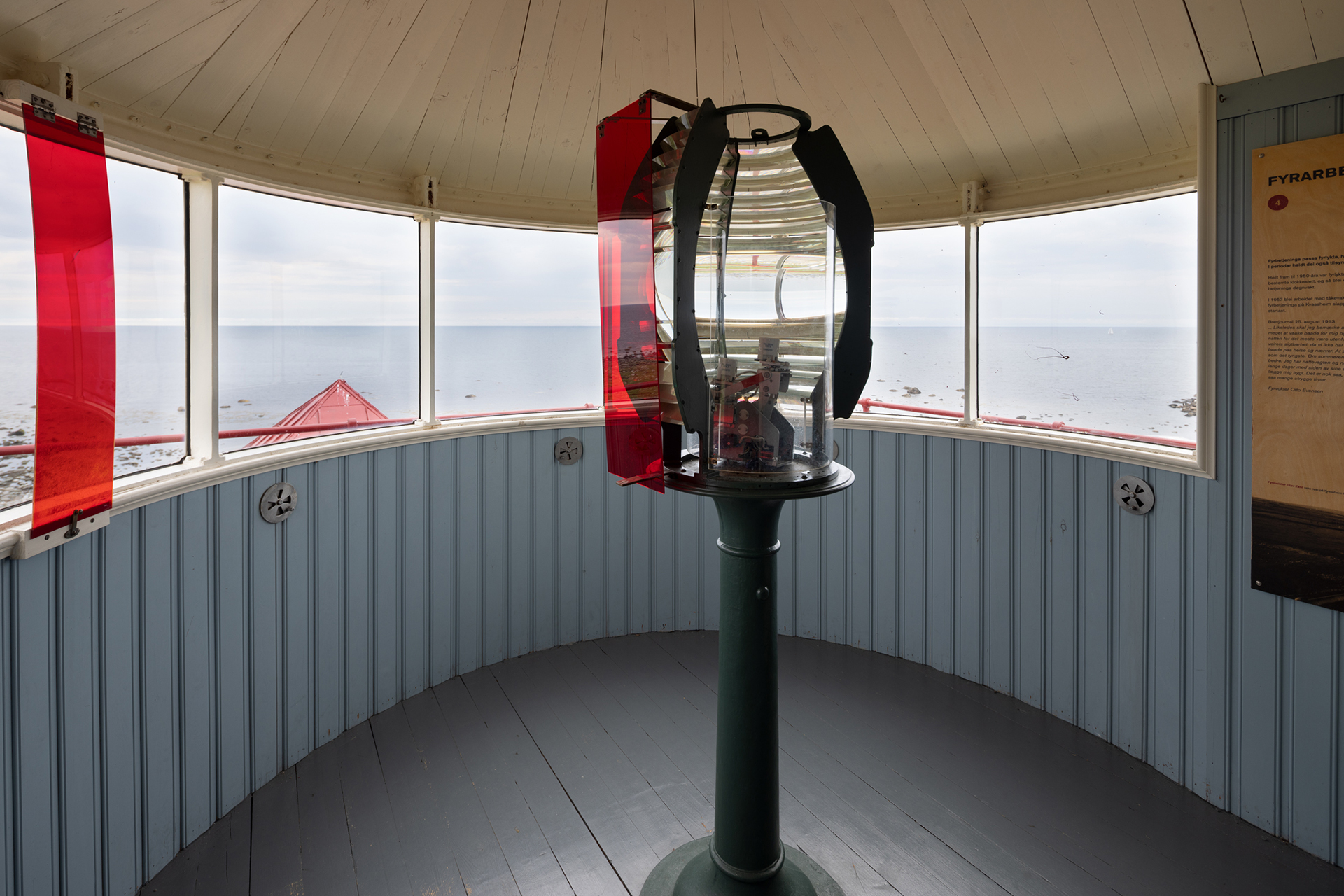 Fra avstandsfyr til nærmiljøfyrtårn 16 Et fyrlykterom med en sentral Fresnel-linse, røde glassruter og vinduer med utsikt over havet og kystlinjen utenfor.