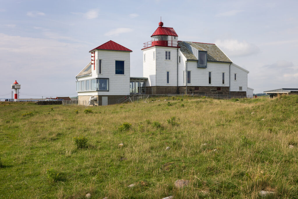 To hvite fyrbygninger med røde tak står på en gresslette, med et mindre fyr synlig i det fjerne til venstre.