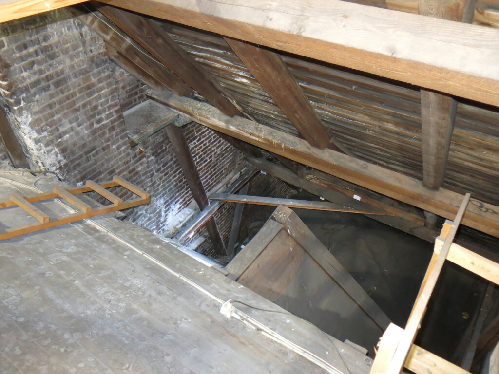 Utsikt over et uinnredet loft på Johanneskirken, med synlige trebjelker, murvegger og et delvis oppbygget eller skadet tregulv.