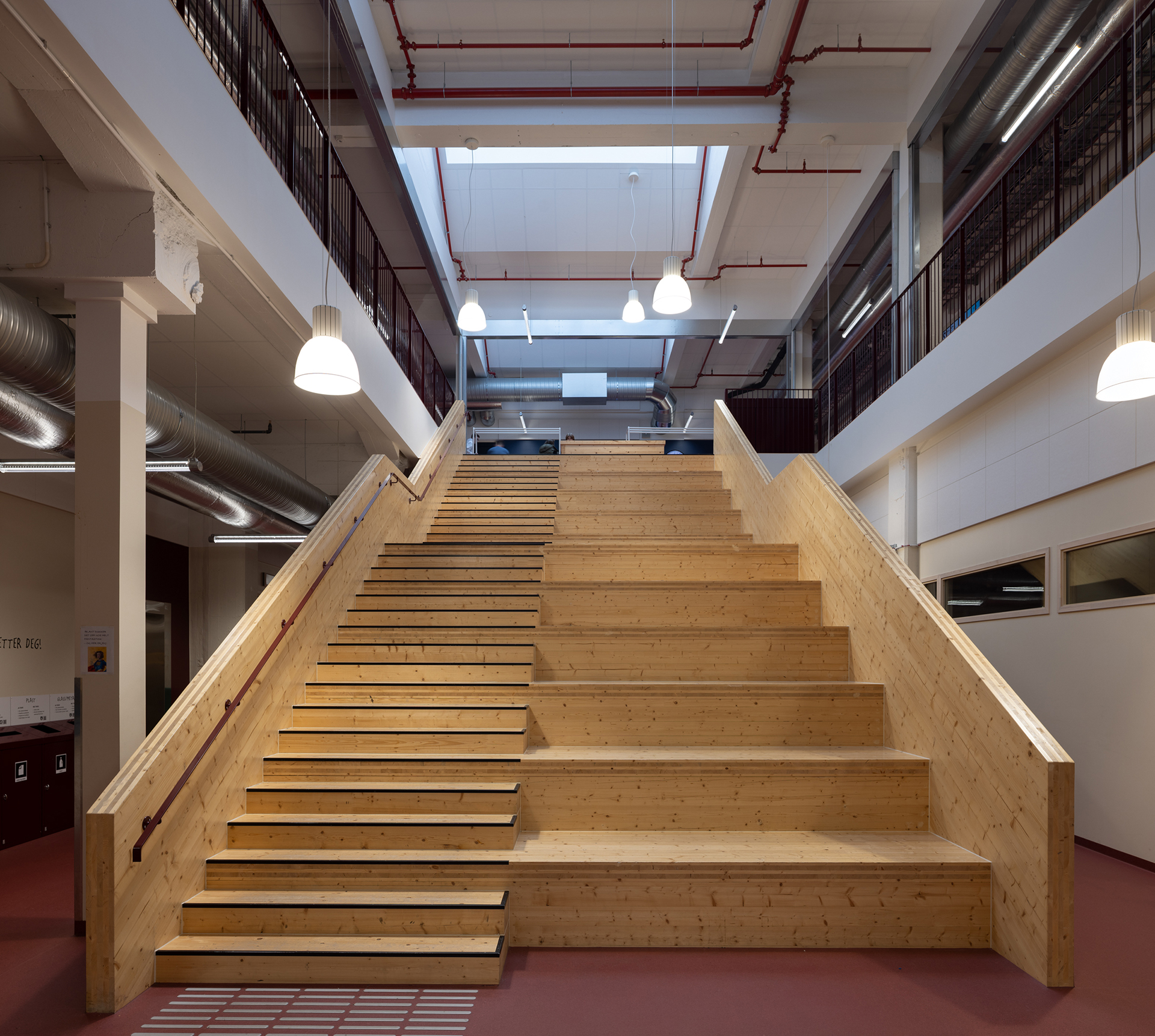 Skulen knyt industrien og byen i hop 8 Bred tretrapp med integrerte sitteplasser i et moderne, åpent interiør med industriell belysning og synlige rør.
