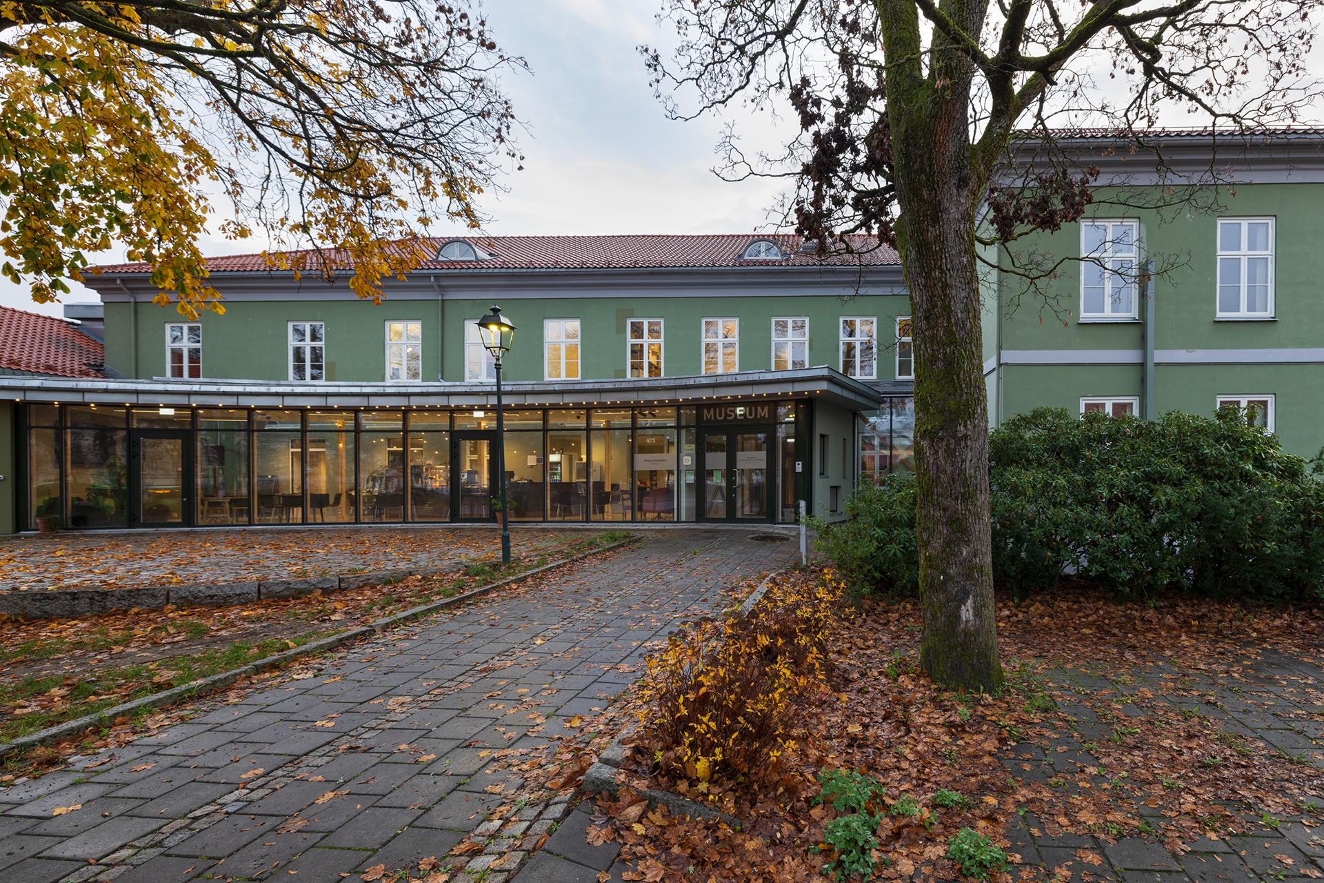 Paleet som opna seg for parken, og for byen 7 En grønn toetasjes bygning med store vinduer og en glassinngang merket Museum, omgitt av høsttrær og løvfall.