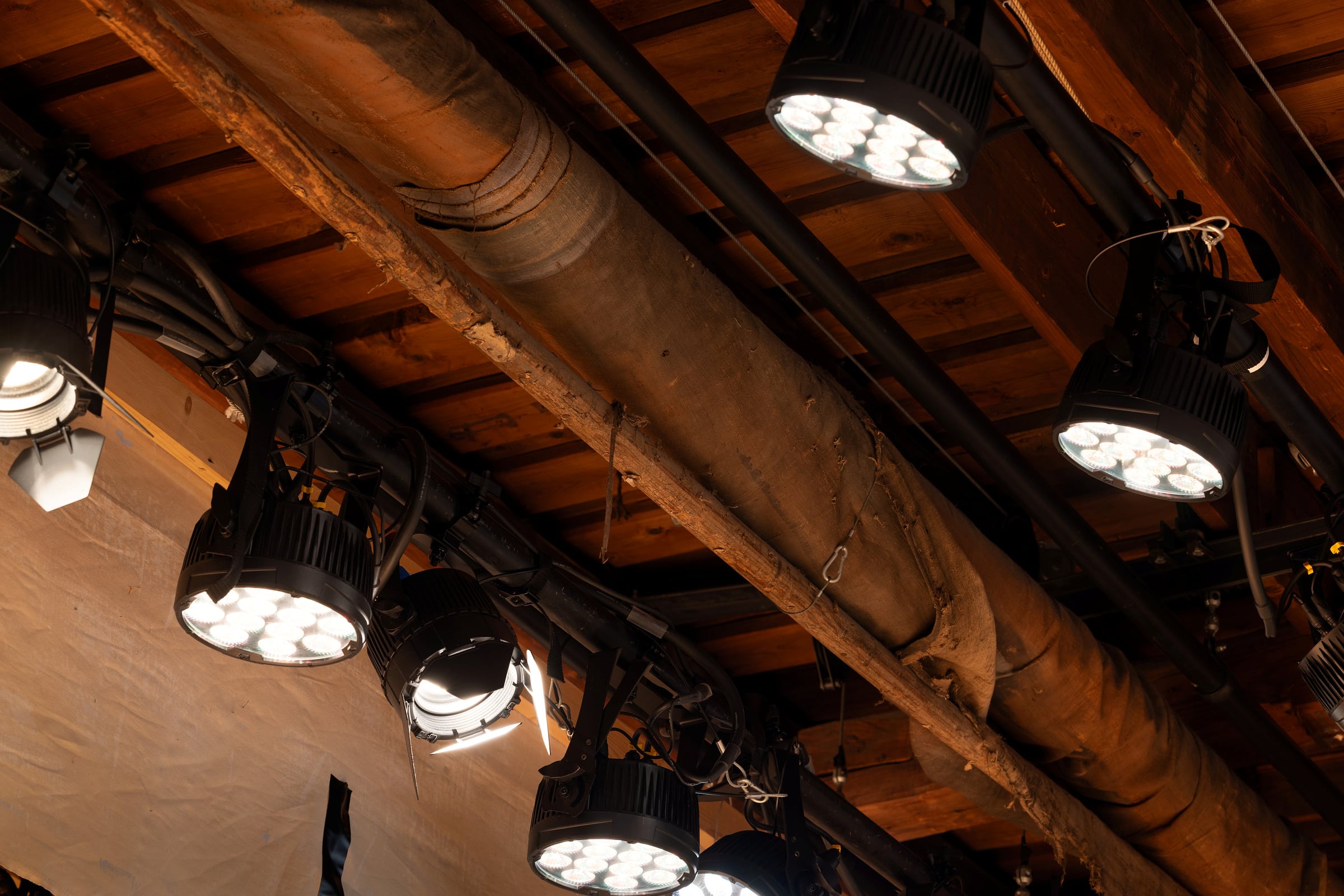 Tryggleik i kulissane 7 Flere scenelamper er montert i et tak med synlige trebjelker og et stort rør i midten, som lyser opp området under.