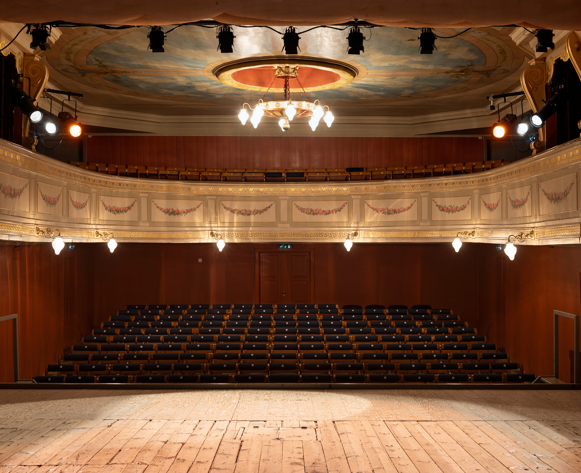 Rigga med både tradisjonelle og moderne løysingar 6 Utsikt fra en teaterscene med tomme publikumsplasser, utsmykket balkong og dekorativt tak med scenelyset slått på.
