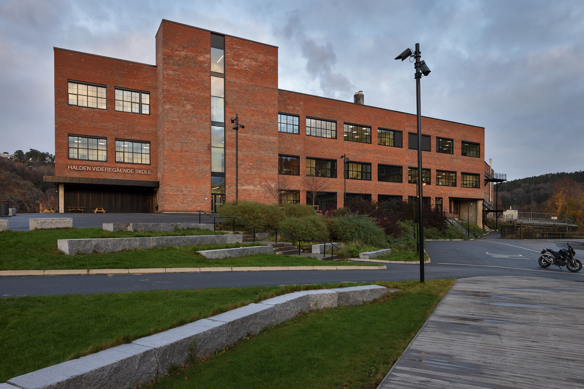 Skulen knyt industrien og byen i hop 7 En stor mursteinsbygning med flere vinduer med påskriften Halden Videregående Skole, omgitt av anlagte stier, gress og en parkert motorsykkel.