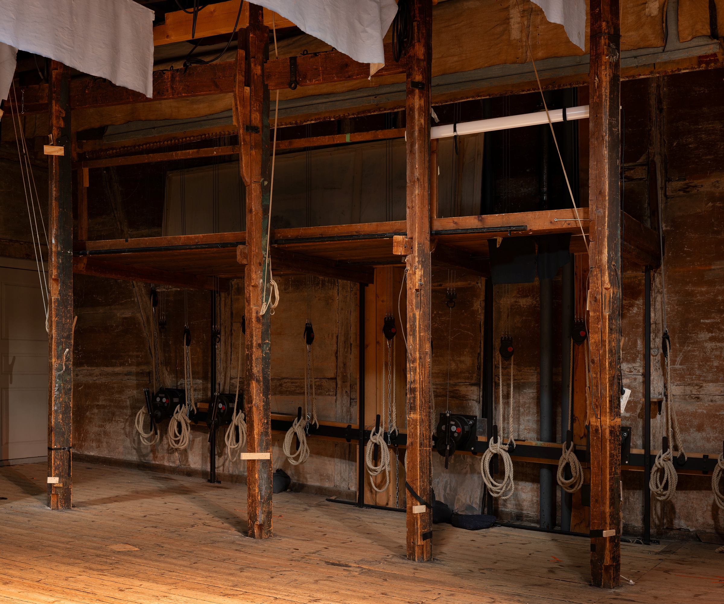 Rigga med både tradisjonelle og moderne løysingar 7 Sceneriggingsområde i tre med synlige bjelker, tauverk og taljer mot en slitt trevegg, typisk for utstyr bak scenen på et teater.