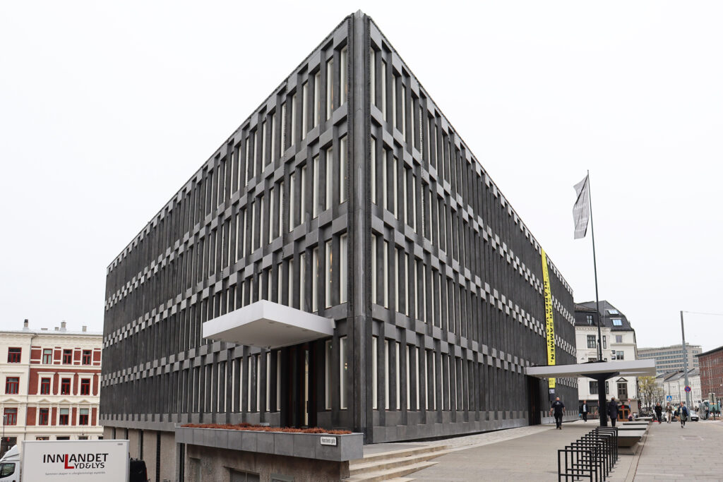 Den tidligere amerikanske ambassaden. En stor, rektangulær, modernistisk bygning med en rutenettlignende fasade med smale, vertikale vinduer og et utkraget inngangstak. Mennesker og et flagg er synlige på utsiden.