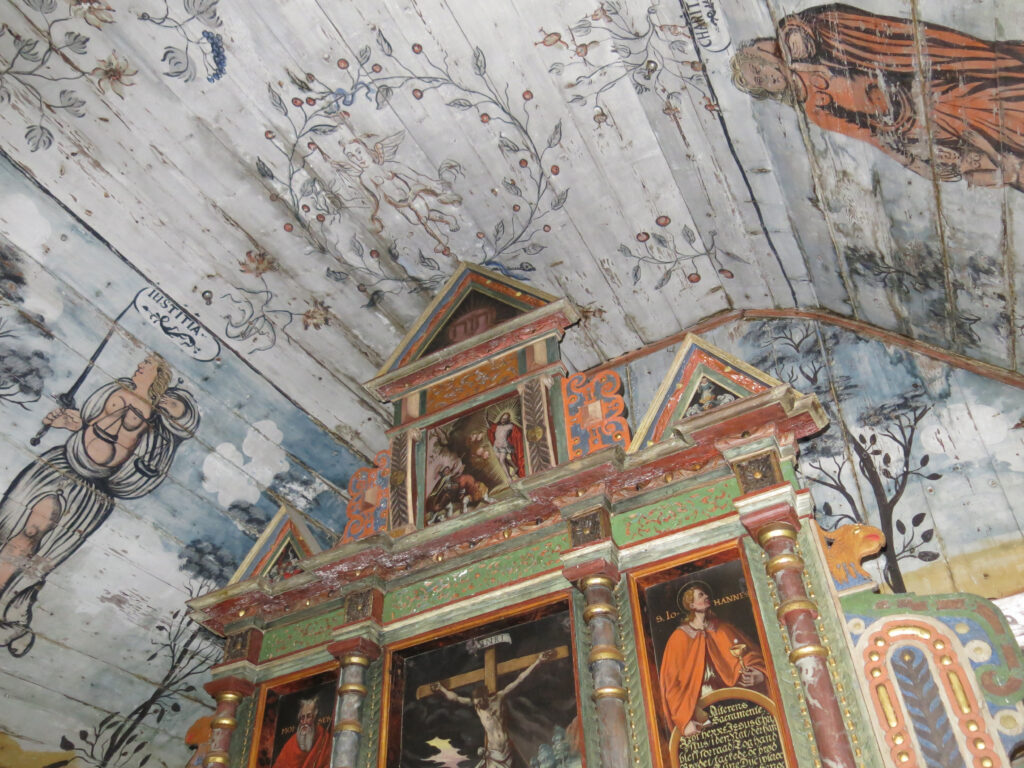 Bemalt kirketak og alter i tre med religiøse ikoner, blomstermotiver og figurer på veggene og i det hvelvede taket.