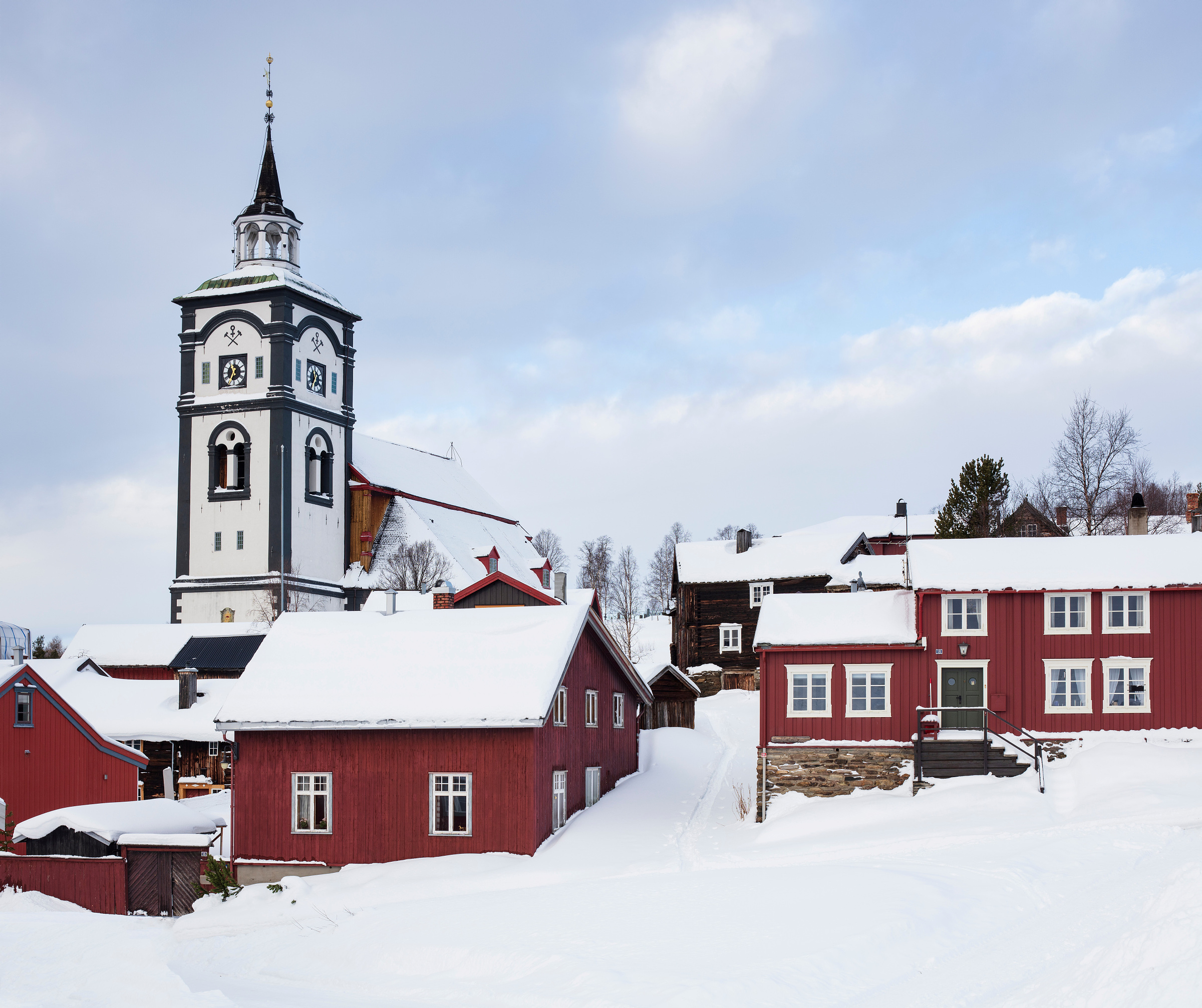 Mørkstugata på Røros med trebygninger og tårnet på Røros kirke under en overskyet himmel.
