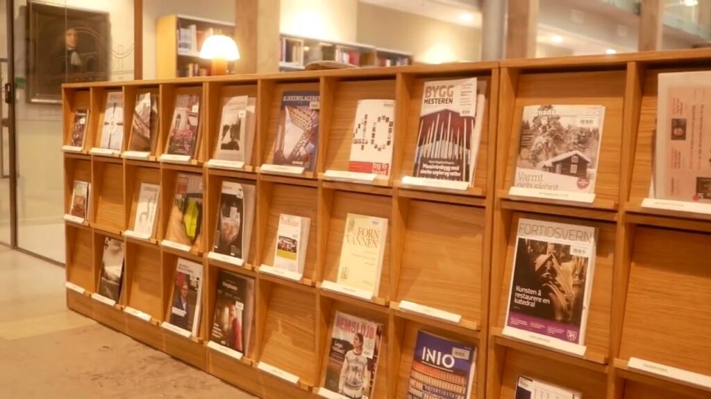 En magasinhylle i tre i et bibliotek viser ulike magasiner og tidsskrifter, sirlig plassert i individuelle spalter.