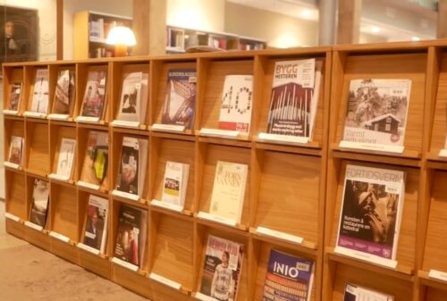En magasinhylle i tre i et bibliotek viser ulike magasiner og tidsskrifter, sirlig plassert i individuelle spalter.