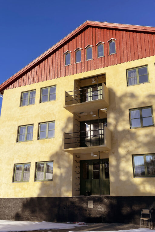 En gul og rød treetasjes bygård med balkonger og mange vinduer, fotografert på en solrik dag.
