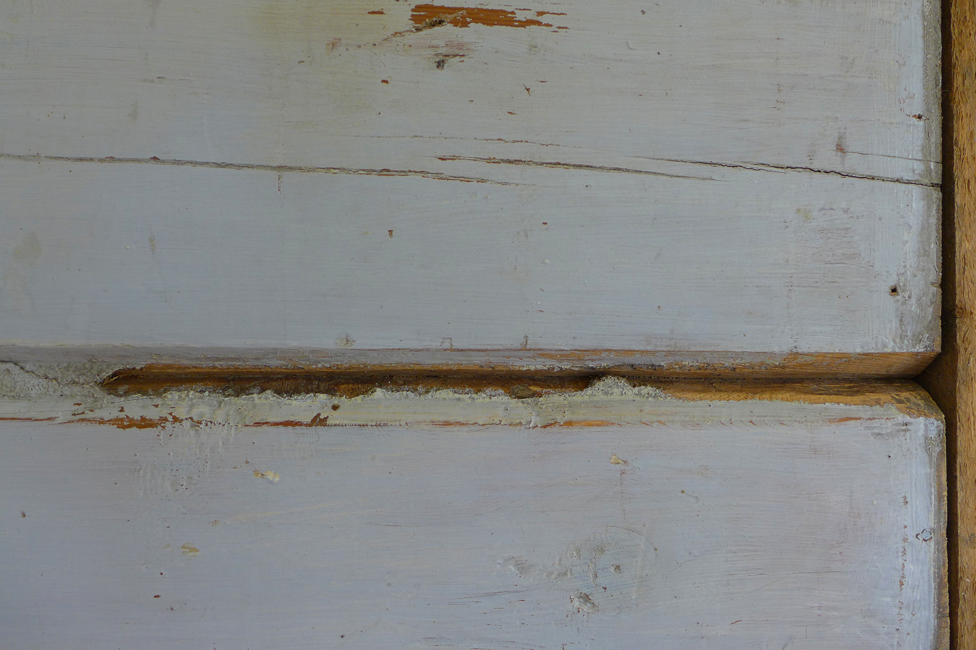 Nærbilde av to forvitrede treplanker med synlige sprekker, avskallet maling og noe blottlagt treverk langs kantene.