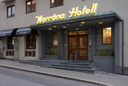 Eksempelsamling 3 Inngangspartiet til Norrøna Hotell med neonskilt, grønn markise, glassdører og to opplyste glassmalerier på hver side, beliggende i en stille gate.