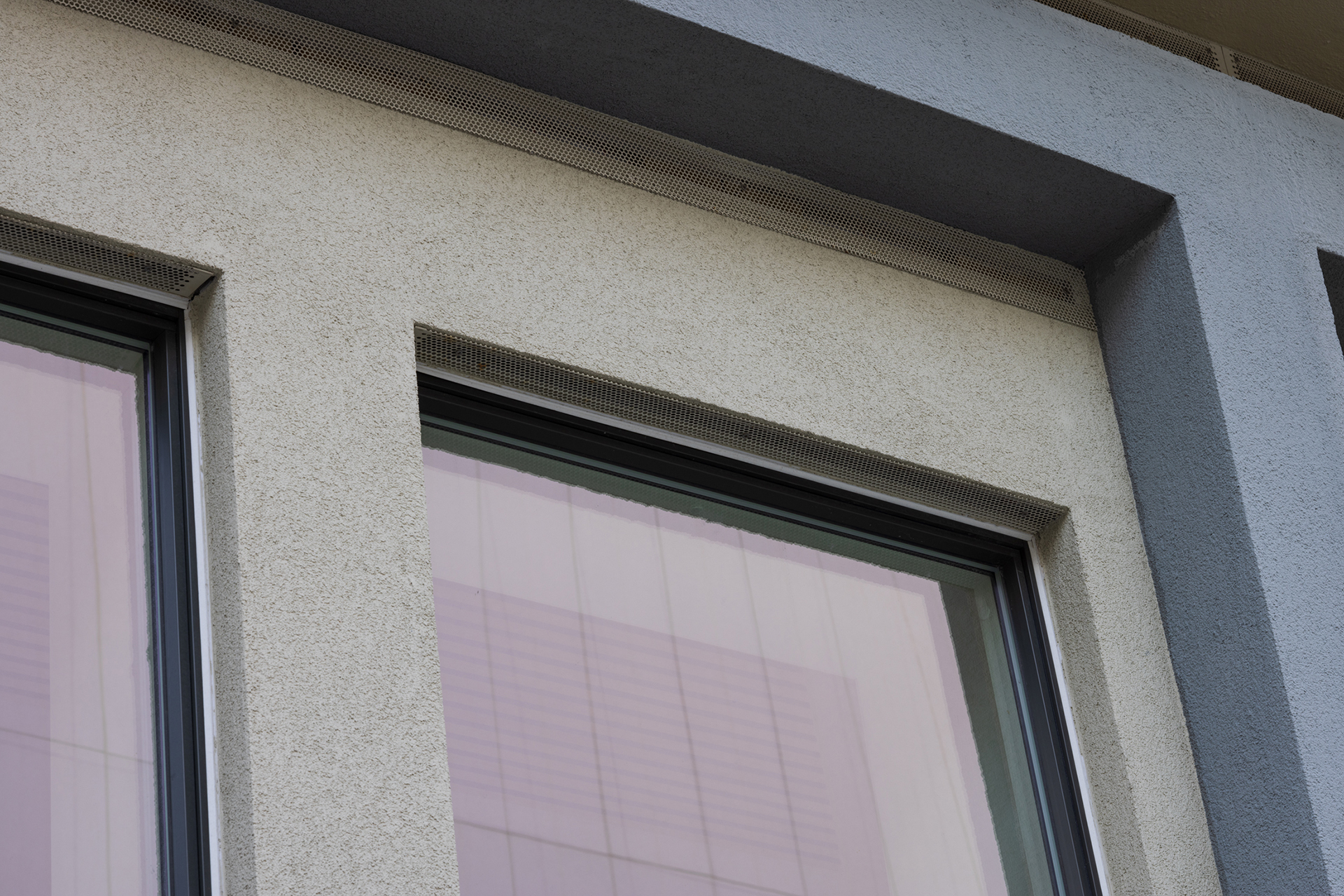 Nærbilde av to moderne bygningsvinduer med reflekterende glass og strukturerte grå og beige yttervegger.