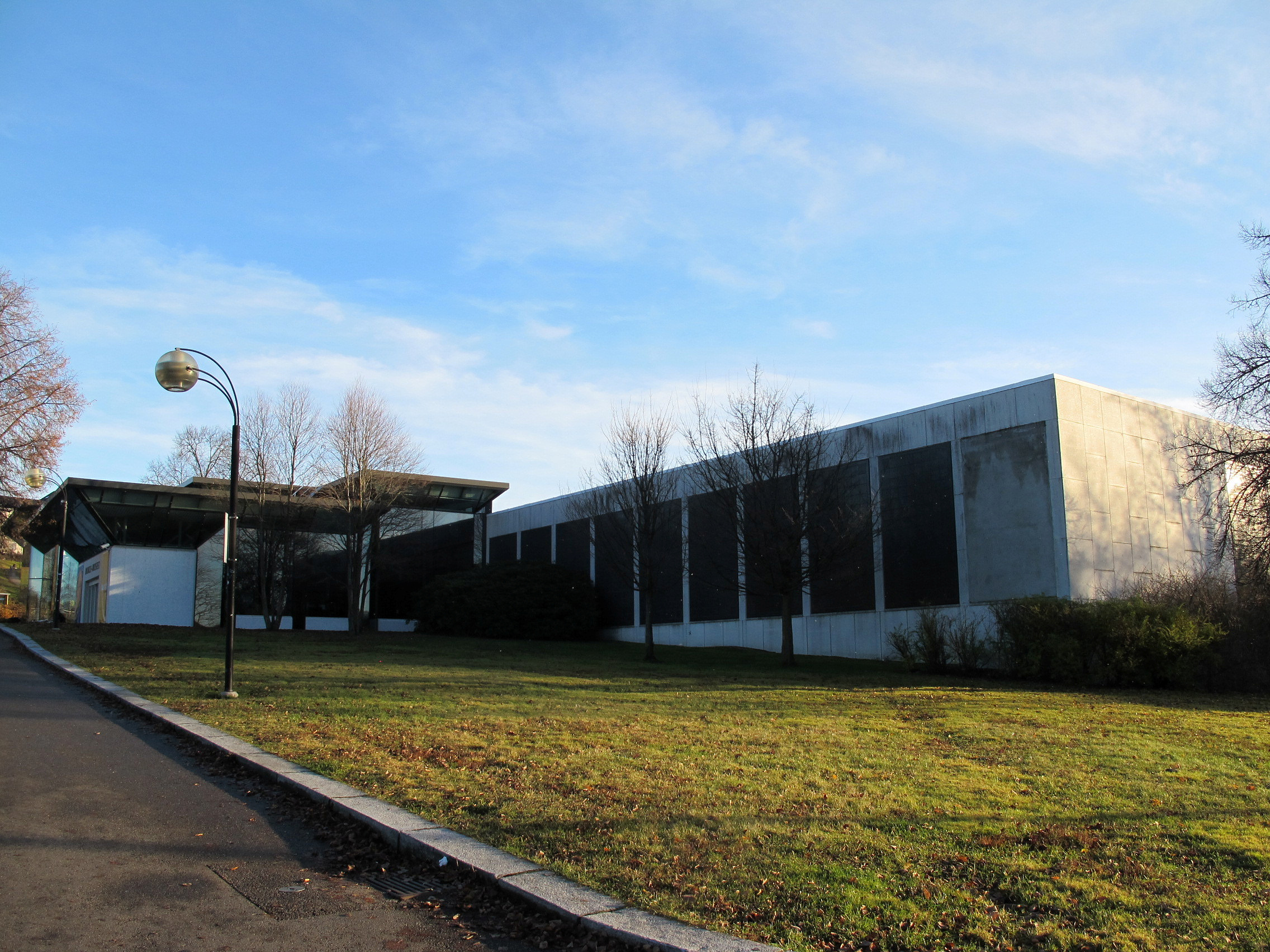 Riksantikvaren tildeler fem forskningsoppdrag for 2026 1 En moderne, rektangulær bygning med store vinduer og betongvegger ligger ved siden av en gressplen under en skyfri himmel.