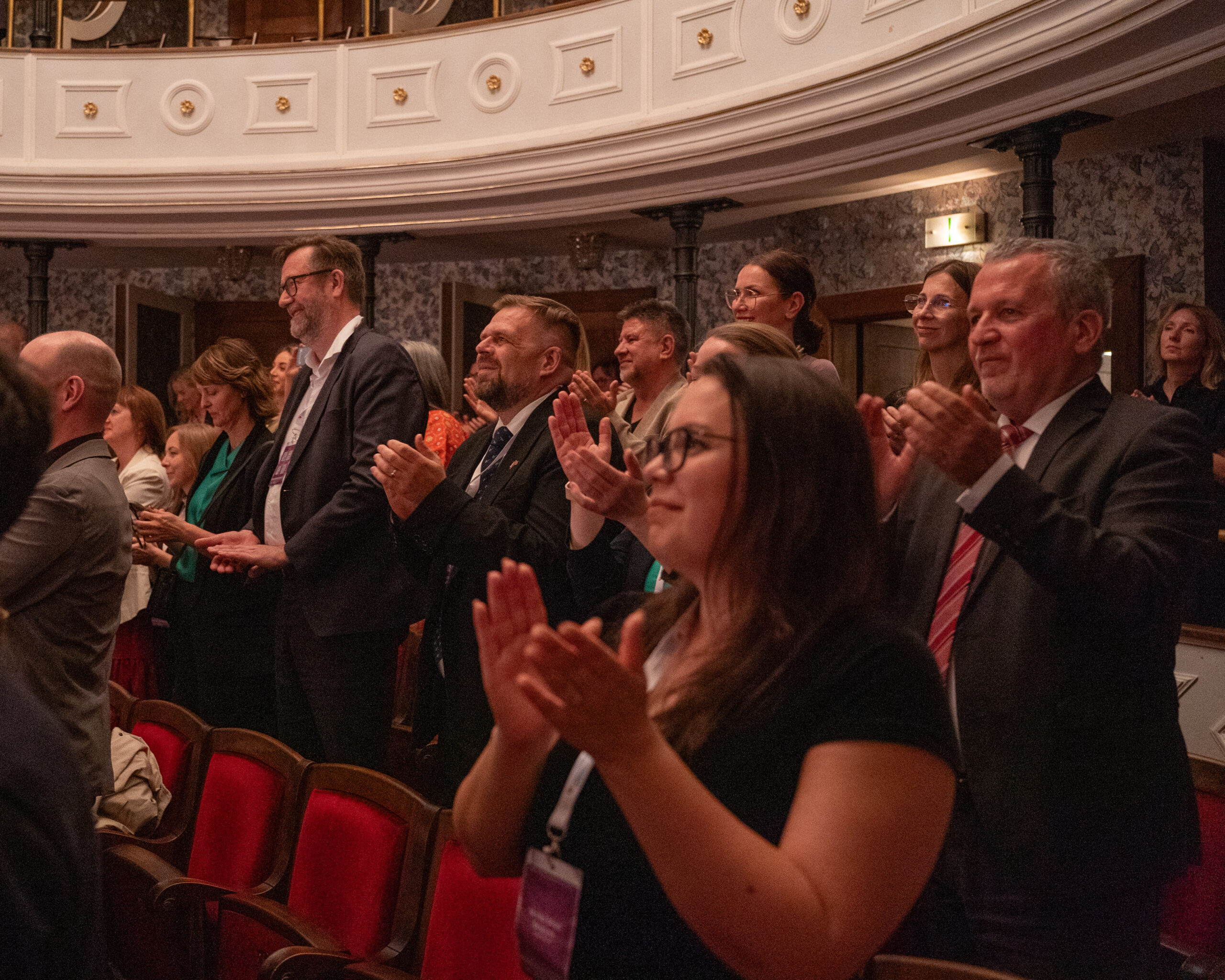 Kulturprogrammet i Slovakia er opna 1 En gruppe mennesker i formelle antrekk står og klapper i et auditorium med røde seter og utsmykkede hvite balkongdetaljer.