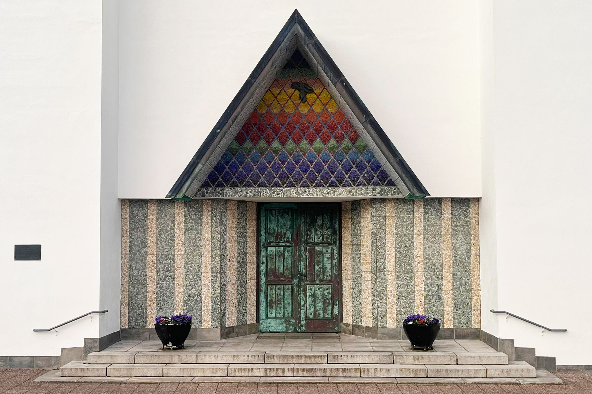 Å nytte handlingsrommet 6 Symmetrisk inngangsparti med grønn dobbeltdør, stripete vegger, trekantet vindu med glassmalerier og to svarte blomsterpotter på hver side av trappen.