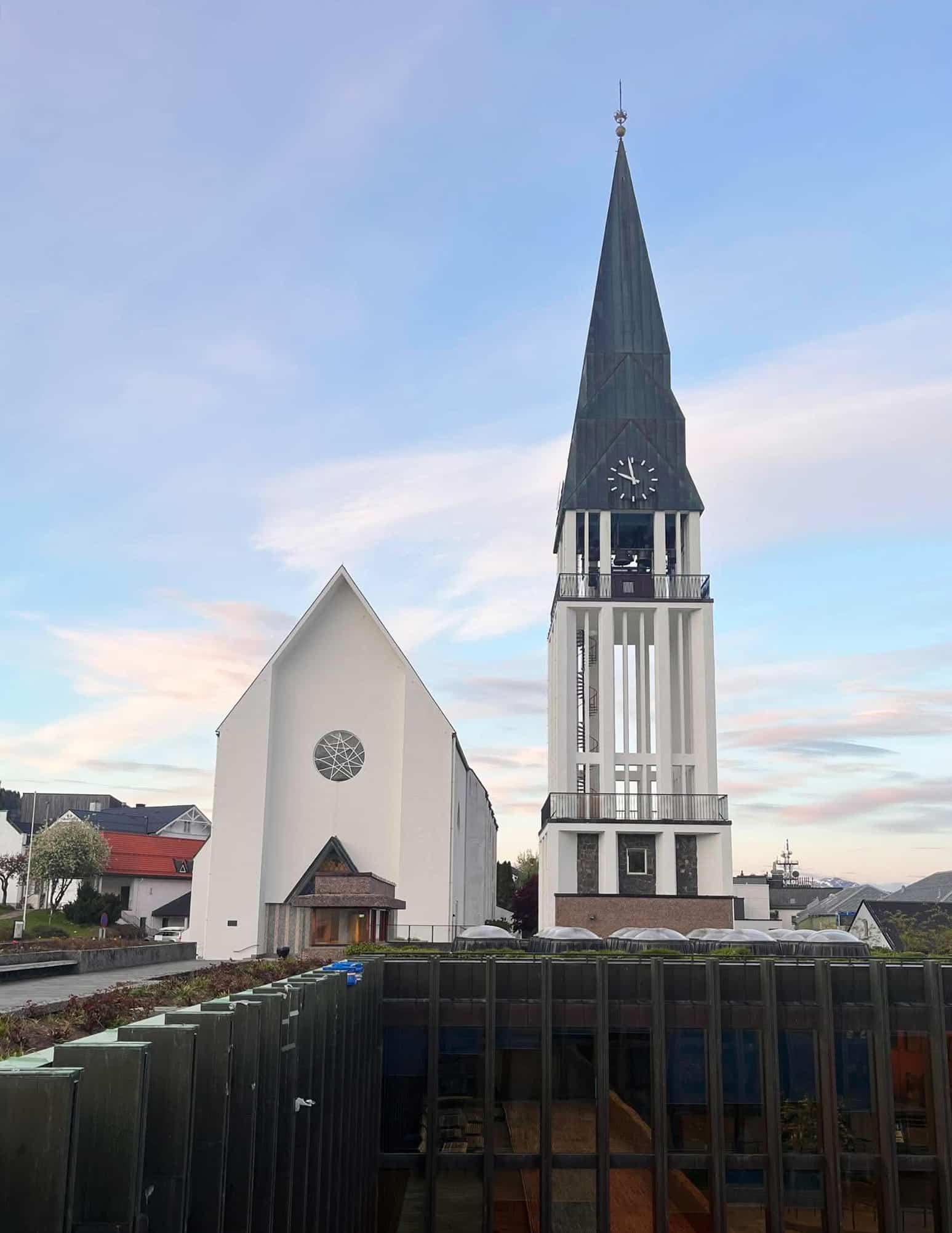 Å nytte handlingsrommet 9 En moderne kirke med et høyt klokketårn står ved siden av en hvit bygning, med glasspanelkonstruksjoner og hustak i forgrunnen under en delvis overskyet himmel.