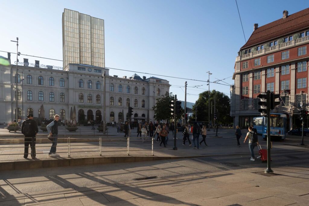 Et torg med folk som går rundt, en trikk og historiske bygninger under en klar, blå himmel i bakgrunnen.