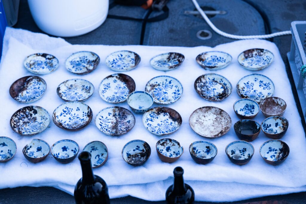 A collection of small, blue and white patterned ceramic bowls, some with damage, placed on a white cloth.