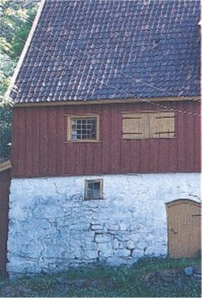 Vedlikehold av grunnmur 3 Et gammelt hus med nedre vegger av hvit stein, en øvre del av rødt treverk, et tak med takstein, små vinduer og en tredør.