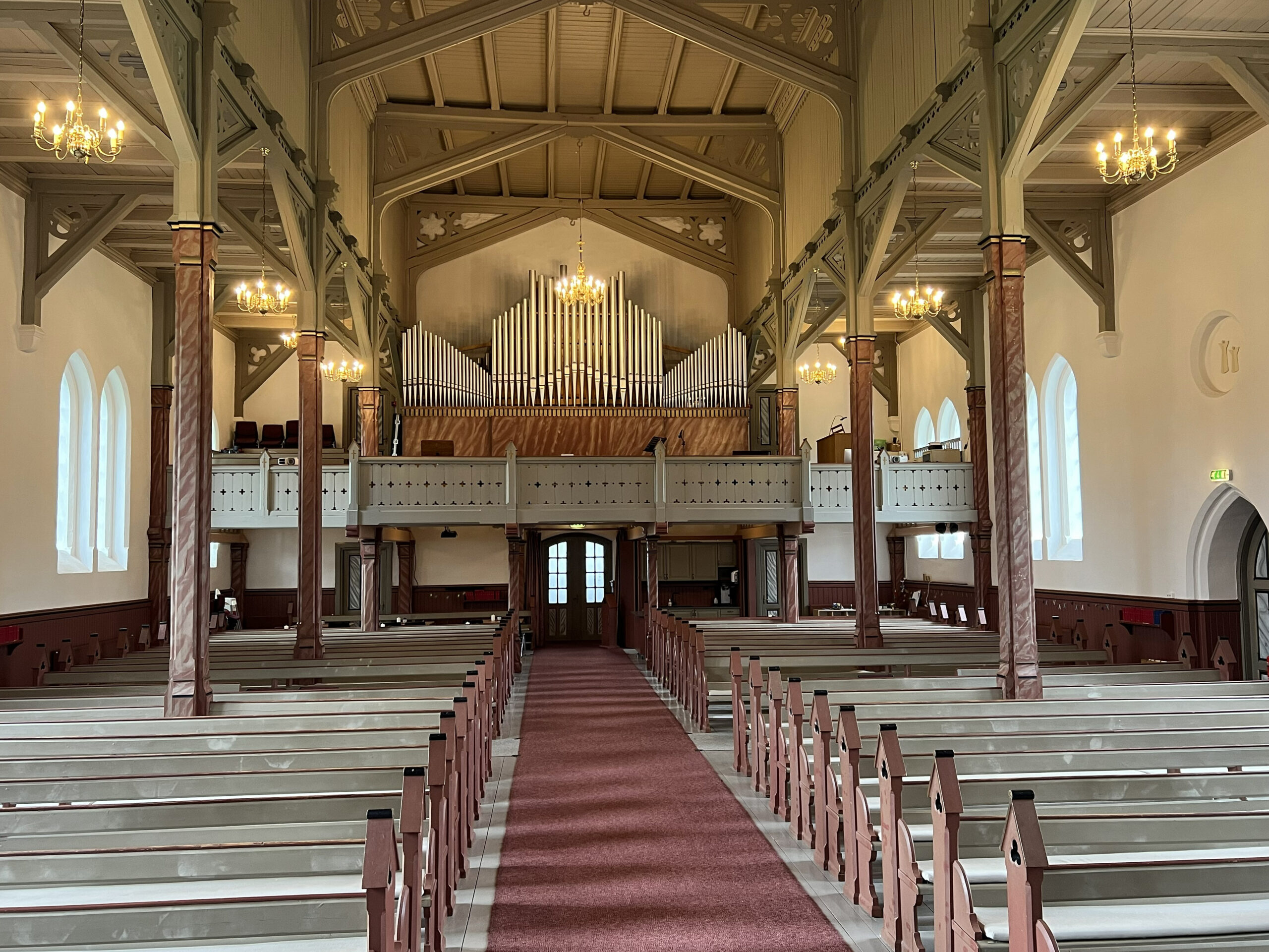 Interiøret i en kirke med trebenker, lysekroner, høye tak, buede vinduer og et stort pipeorgel på en balkong helt bakerst i kirken.