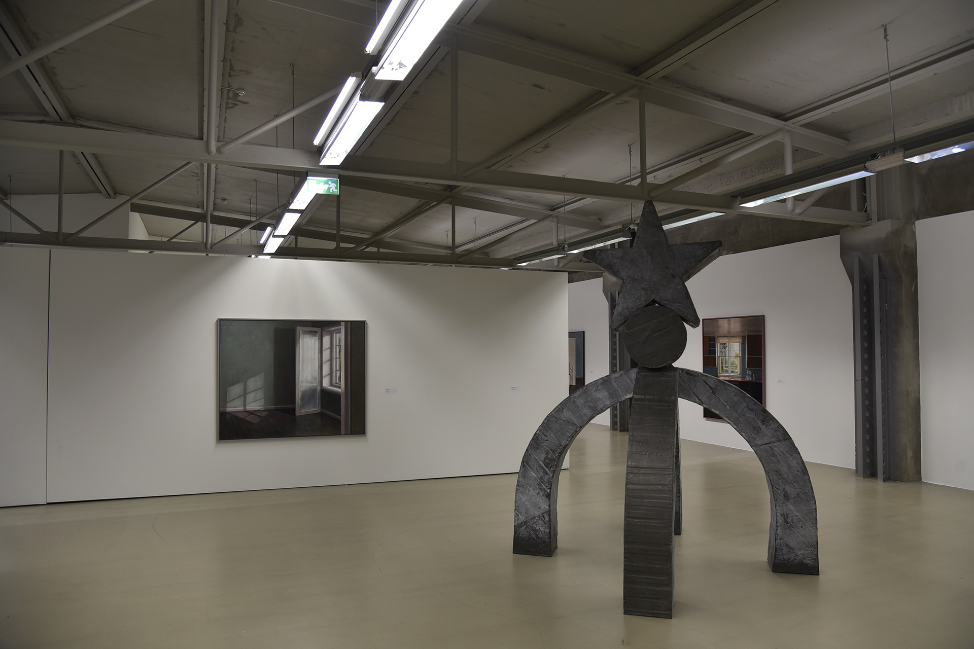 Et galleri for moderne kunst viser frem en stor metallskulptur og et innrammet maleri på hvite vegger under lysrør.