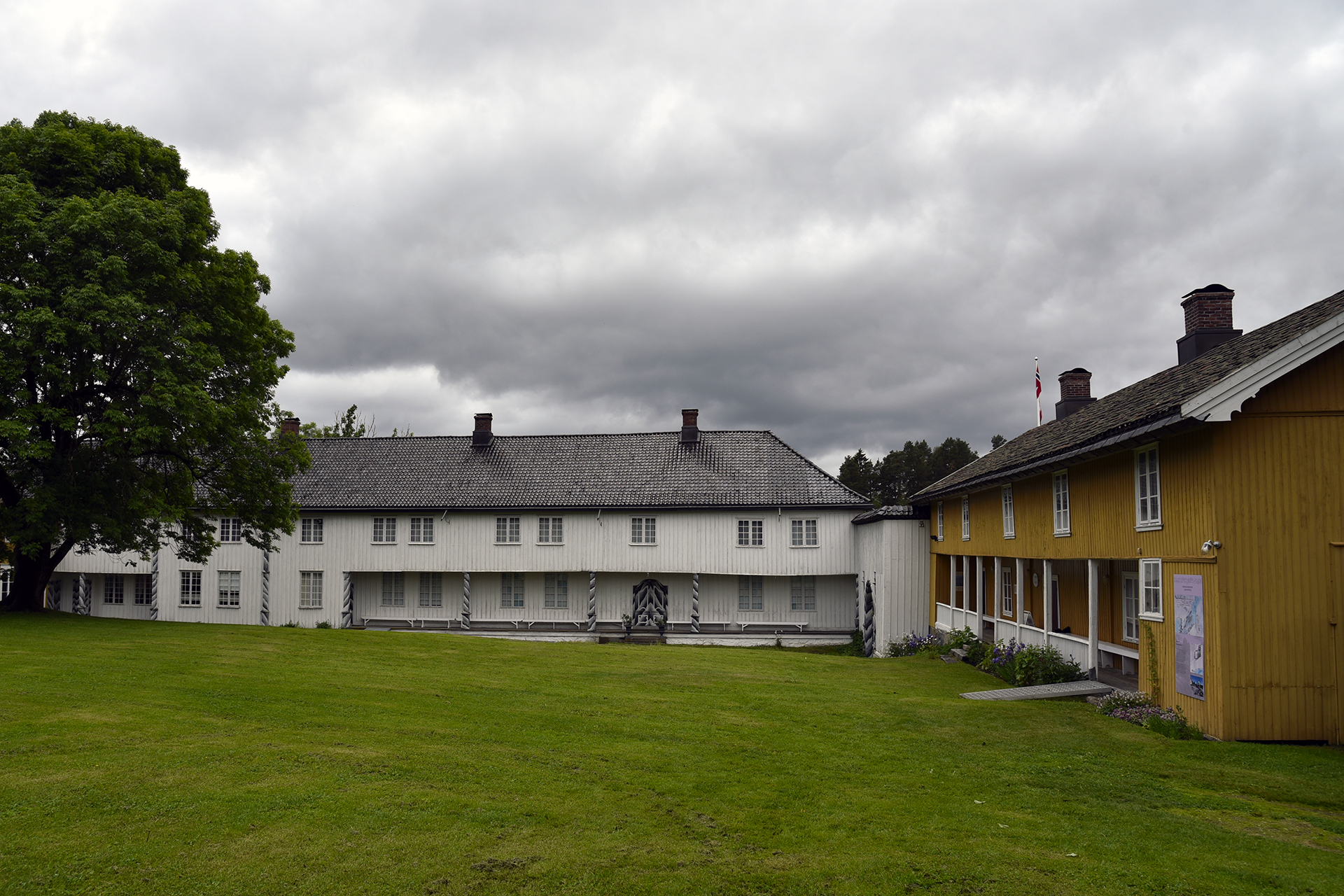 Å verne verdiane utan å skade 6 To tradisjonelle trebygninger, den ene hvit og den andre gul, vender ut mot en gresskledd gårdsplass under en overskyet himmel.
