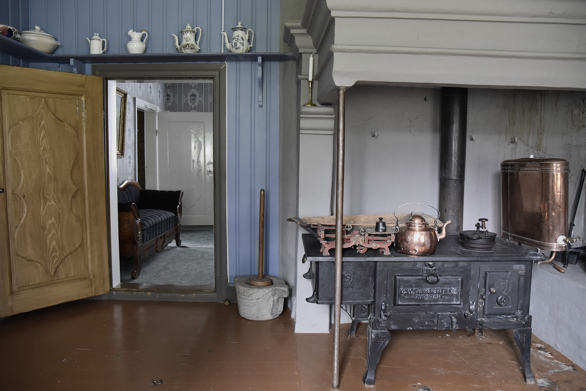Å verne verdiane utan å skade 11 Et kjøkken i vintage-stil har en støpejernsovn med kobberkjeler, tregulv og en åpen dør som fører inn til en stue med en stripete sofa.