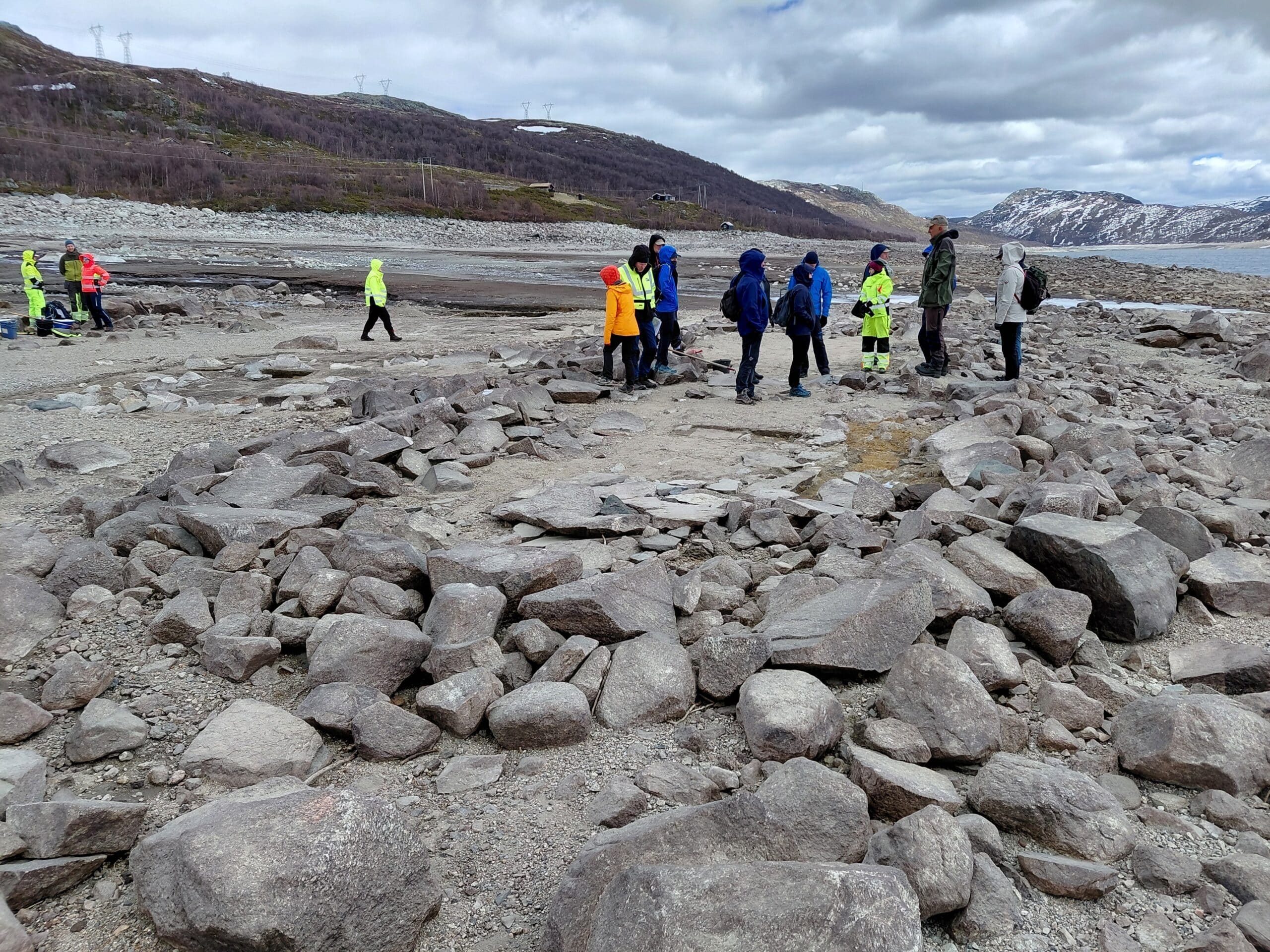Sektoravgiftsseminar 1 En gruppe kulturmiljøforvaltere på befaring står i friluftsklær ved tuften på Langegard ved Strandavatn, med åser i bakgrunnen.
