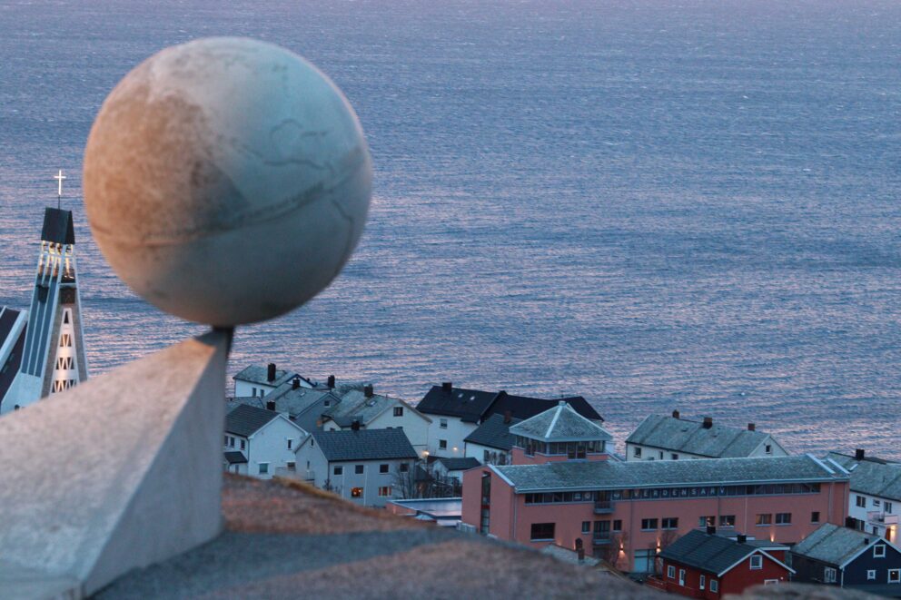 Verdsarvutstillinga på plass i Hammerfest 7 En steinkule på en sokkel med utsikt over en kystby med en kirke og havet.