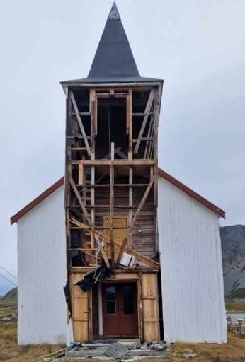 En hvit kirke med et skadet, delvis åpent tårn foran.