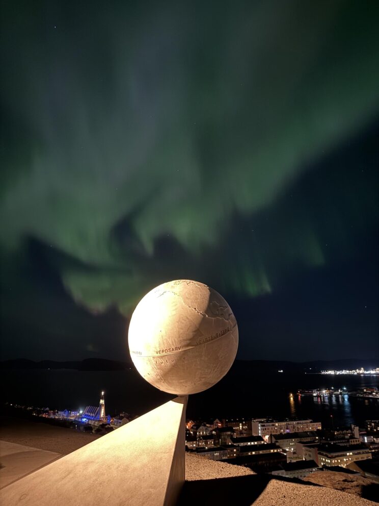 Verdsarvutstillinga på plass i Hammerfest 5 En skulptur i form av en jordklode, opplyst mot en himmel med nordlys, med utsikt over kystbyen Hammerfest.